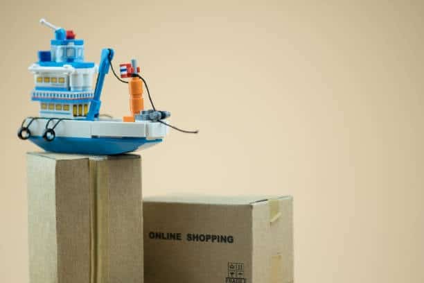 Miniature cargo ship model placed on cardboard boxes, symbolizing detention and demurrage charges in shipping logistics.