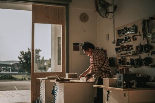 A skilled craftsman working diligently in his well-organized workshop, focusing on a wooden piece, illustrating the precision and dedication in handmade craftsmanship.
