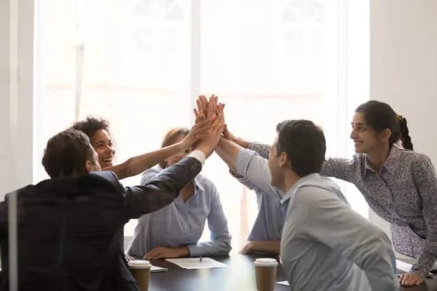 A diverse group of professionals giving a high-five over a meeting table, symbolizing successful teamwork in managing customs clearance processes.