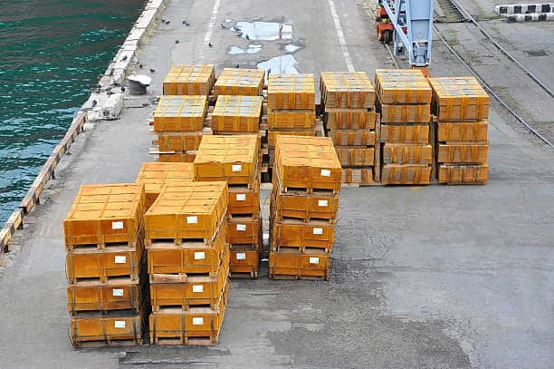 Stacks of green and orange shipping containers at a port terminal, illustrating storage scenarios that can result in detention and demurrage fees.