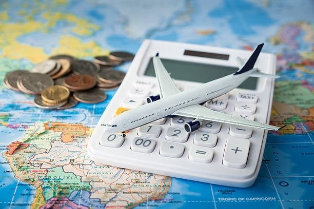 A model airplane on a calculator over a world map with coins, symbolizing the calculation of expenses involved in international shipping and customs clearance.