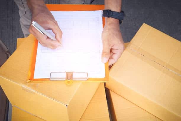 A delivery person verifying and signing customs documentation on a clipboard atop a stack of shipping boxes, highlighting the critical steps in the export process.