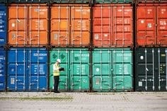 Logistics worker inspecting stacked cargo containers at a container yard, highlighting port operations and demurrage risk due to delays in cargo pickup.