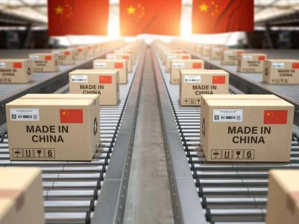 Numerous cardboard boxes labeled 'Made in China' on a conveyor belt, symbolizing mass production and export in global trade under a large Chinese flag.