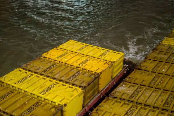 Close-up of yellow shipping containers on a barge moving across water, representing transit processes potentially subject to detention and demurrage charges.