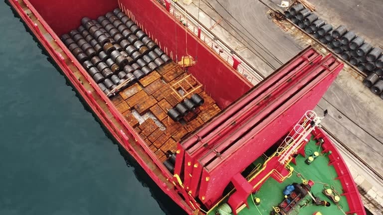 Aerial view of steel barrels being loaded onto a cargo ship for heavy item shipping.