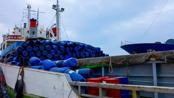 Shipping vessel carrying heavy blue barrels and containers for transport.