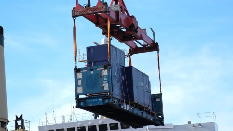 Blue shipping containers being hoisted by crane for loading onto cargo ship.