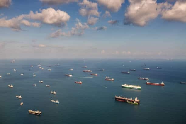 Dozens of cargo ships anchored in the ocean, waiting for berthing space at congested ports, illustrating severe port delays in international shipping.