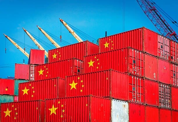 Stacked shipping containers marked with the Chinese flag at a port terminal, representing goods ready for international delivery and highlighting China’s global shipping lead times.