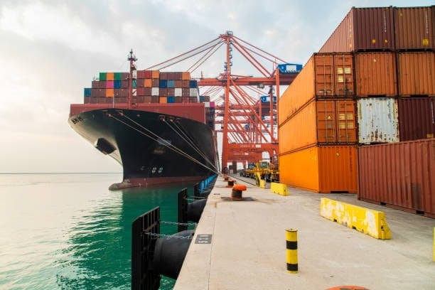 Large container ship docked at a shipping terminal with rows of stacked cargo containers, representing global freight activity and influencing container shipping prices.