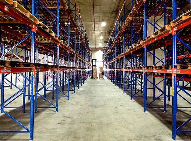 Interior of an empty warehouse with tall racking systems, representing storage and order fulfillment in outbound logistics.