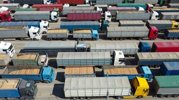 Overhead view of cargo trucks stuck in long queues at a port facility, highlighting the impact of port delays on inland transportation and delivery schedules.
