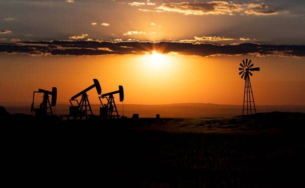 Silhouettes of oil rigs and windmill at sunset, symbolizing energy exports from Germany to the USA.