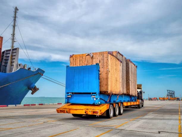 Oversized heavy wooden crate on flatbed trailer for port-to-port shipping.