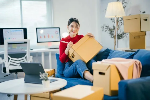 A young entrepreneur happily packing products into a box in a cozy home office setup surrounded by various packed boxes, symbolizing the dynamic nature of home-based e-commerce businesses.