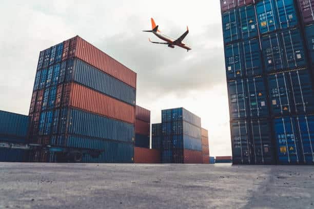 Aircraft flying above container terminal during global freight handling.