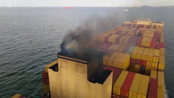 Container ship fully loaded with cargo emitting exhaust smoke at sea, highlighting potential operational issues linked to detention and demurrage charges in maritime transport