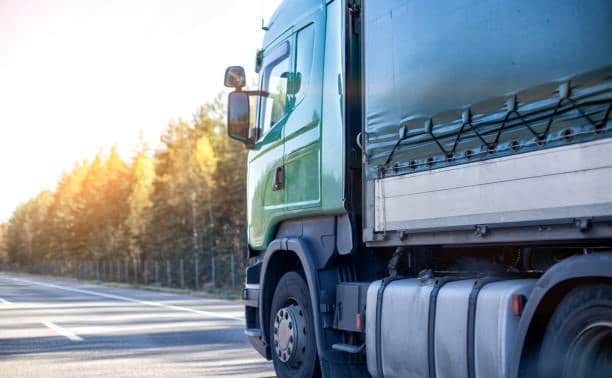 Side view of a green freight truck driving on a highway, representing transportation logistics where per diem fees may apply for delayed container returns.