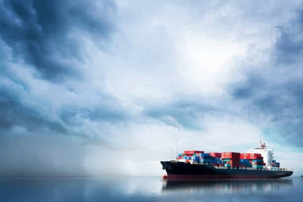 Cargo vessel sailing in calm seas under dramatic skies, symbolizing weather impact on sea freight transit times.