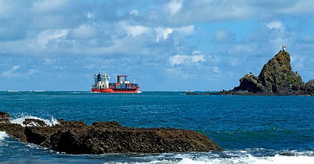 Cargo ship approaching the rocky coastline of New Zealand, illustrating maritime imports.