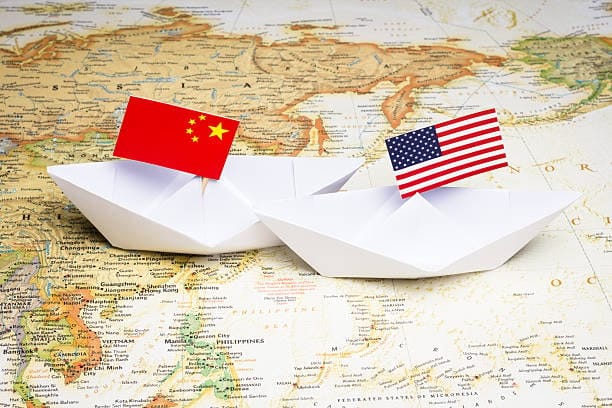 Paper boats with China and US flags placed on map representing international trade and shipping routes.