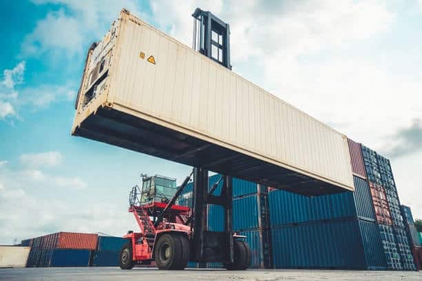 Forklift lifting a shipping container in a freight yard for overseas delivery.