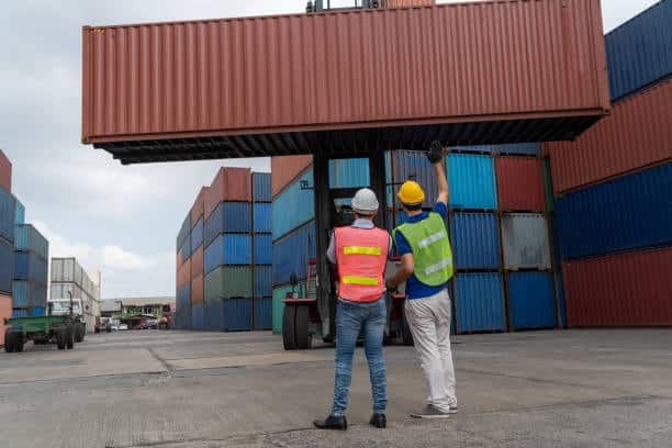Two logistics workers supervising container loading operations for export.