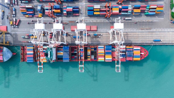 Overhead view of port cranes loading shipping containers for China to USA international freight transport.