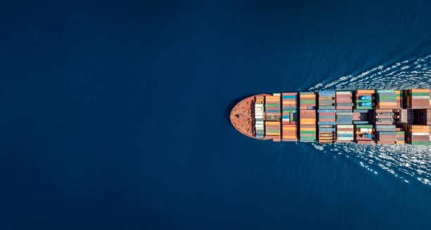 Aerial view of a cargo container ship moving across the ocean, representing global sea freight transit times.