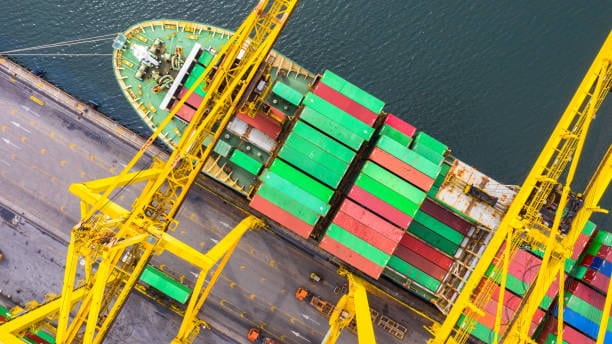Overhead view of container ship being unloaded by large yellow port cranes.