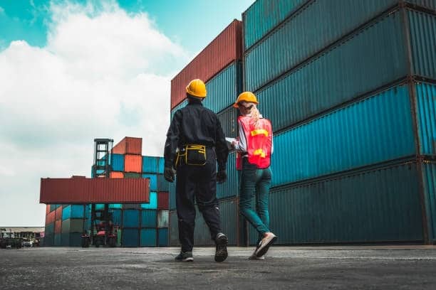 Two workers inspecting stacked containers for overseas shipping logistics.