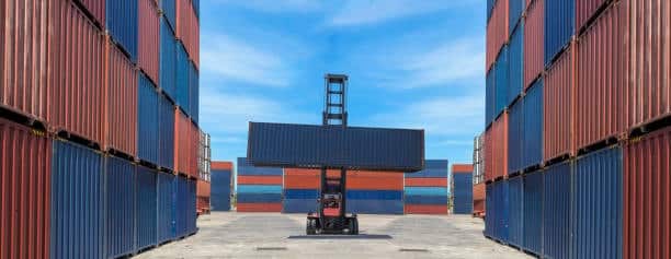 Forklift stacking containers in a shipping yard, showing cargo preparation for door delivery.