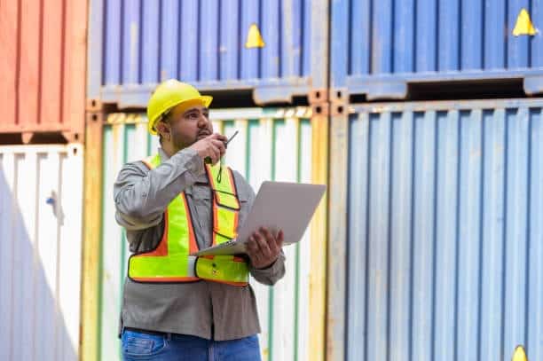 Logistics manager using laptop and radio to coordinate container shipping operations.