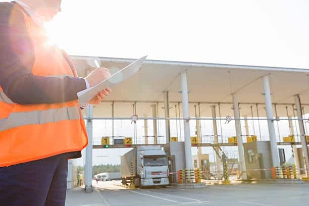 Customs agent reviewing clearance documents near a truck at border inspection point.