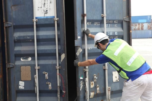 Customs officer opening a shipping container for inspection during clearance.