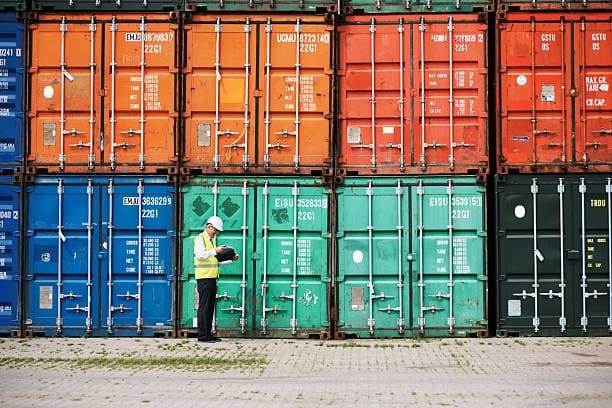 A worker inspecting a row of colorful shipping containers, highlighting the logistical aspect of customs duties enforcement in international trade.