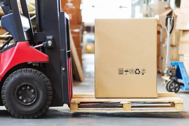 Forklift loading a large cardboard box onto a pallet for big box shipping.