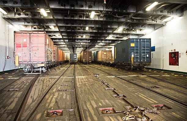 Railcars with freight containers secured on a cargo vessel for transport.