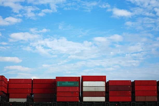 Stacked green containers ready for outbound freight export under blue sky.