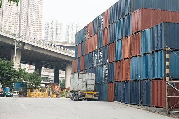 Shipping containers stacked in urban freight yard awaiting outbound dispatch.