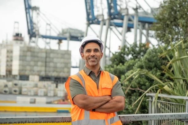 Smiling logistics worker in high-visibility vest at container port.