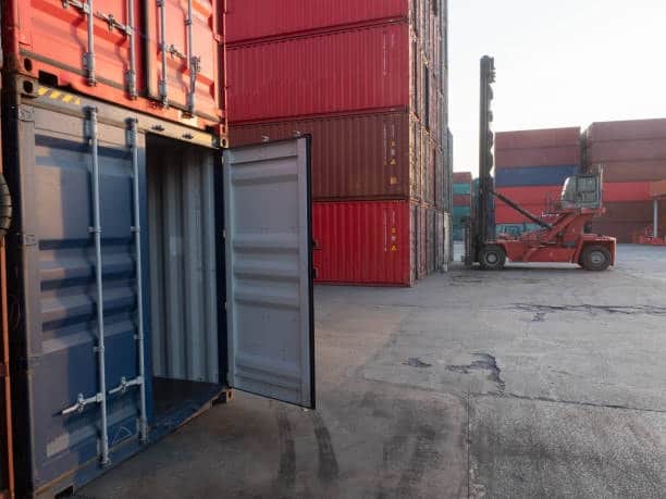 Open shipping container in a container yard, indicating loading or unloading during port-to-door delivery.