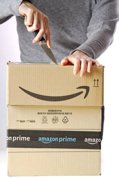 Person using a knife to open an Amazon Prime package showing FBA-compliant packaging details.