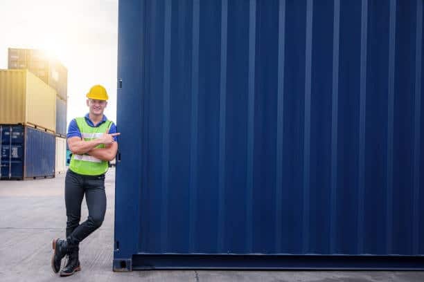Logistics worker standing by a shipping container in a yard, representing port-to-door coordination.