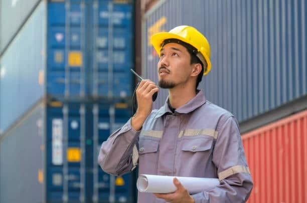Supervisor at container terminal using walkie-talkie to manage overseas shipments.