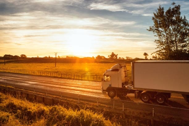 Freight truck transporting goods across a rural New Zealand highway at sunset.
