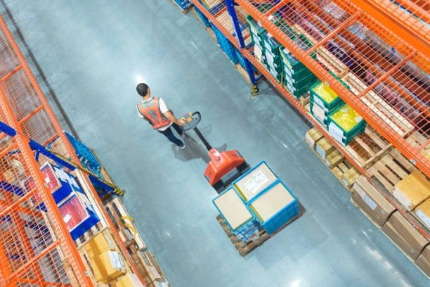 Warehouse worker using a pallet jack to move large boxes for shipping.
