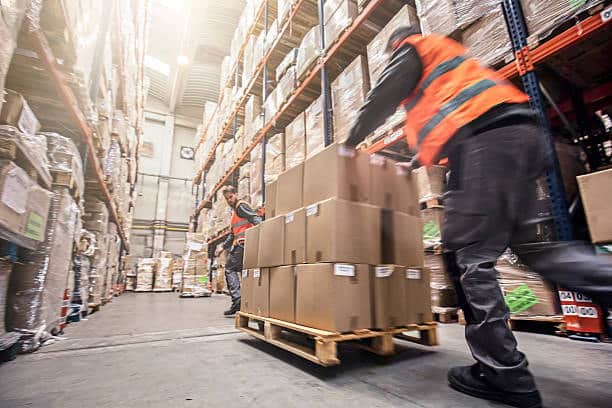Workers moving heavy big box shipments on pallets inside a logistics warehouse.