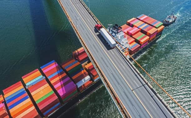 Cargo ship carrying containers under bridge, symbolizing international freight shipping